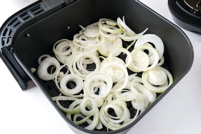raw onion rings sitting in black air fryer basket on counter top.
