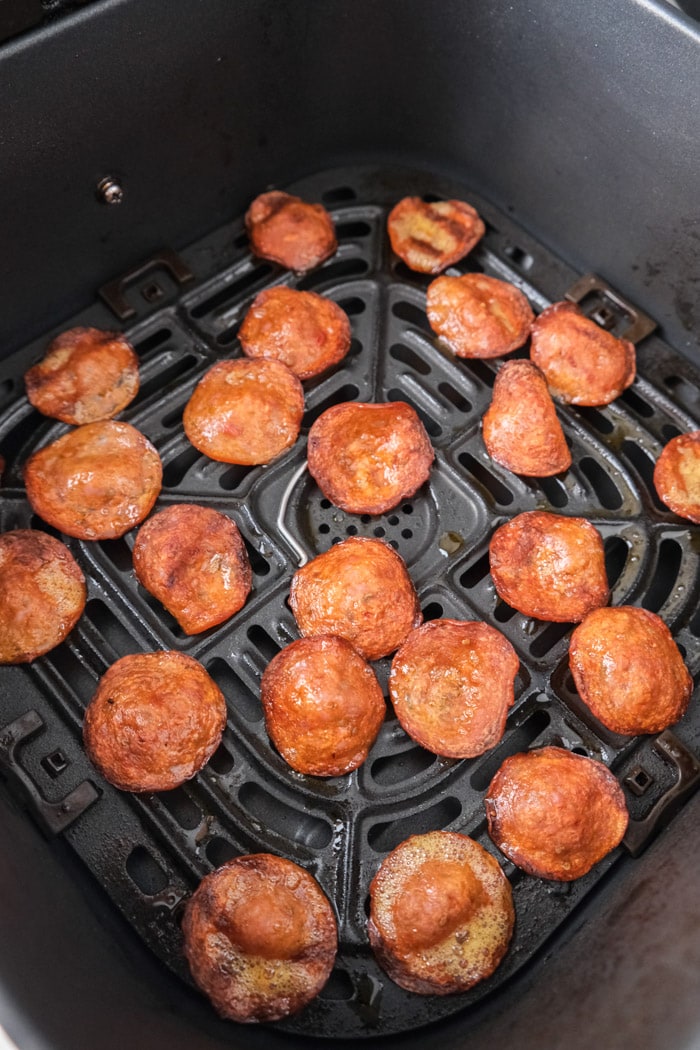 crispy pepperoni chips cooking in black air fryer tray on counter.