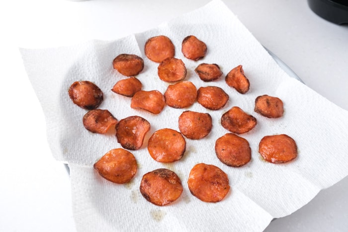 crispy pepperoni sitting on paper towel on white plate on counter top in kitchen.