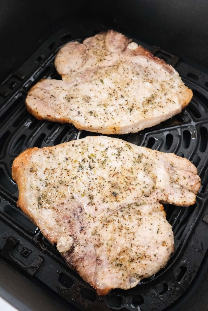 two cooked pock chops with spices on top in black air fryer tray.