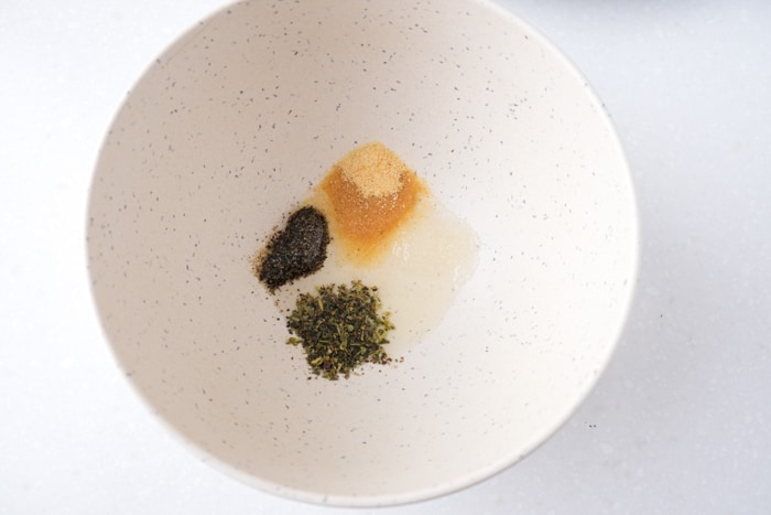 spices and oil in white mixing bowl on white counter top.