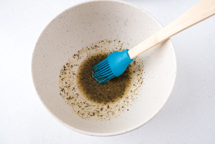 blue tipped cooking brush sticking out of white mixing bowl filled with spice mix sitting on white counter.