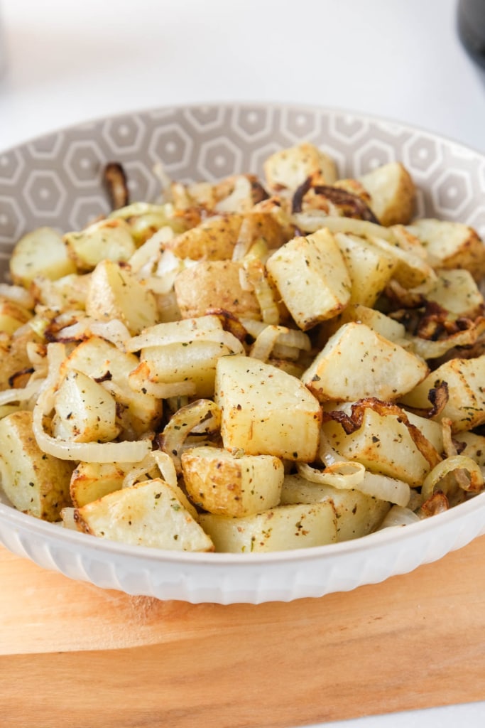 air fried potatoes and onions in bowl on wooden board with white counter underneath.
