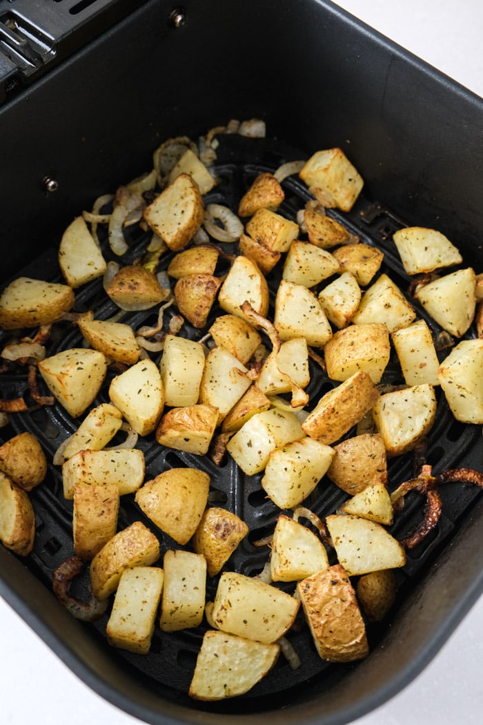 cooked potatoes and onions in black air fryer basket on counter.