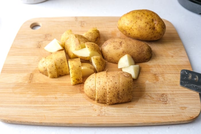 raw potatoes cut on wooden cutting board with sharp knife beside on white counter.