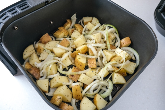 raw cut potatoes and onions in black air fryer tray on white counter top