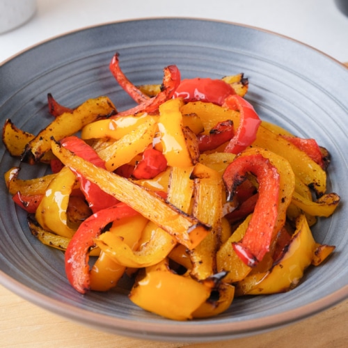 cooked strips of yellow and red peppers in blue bowl on wooden board in kitchen.