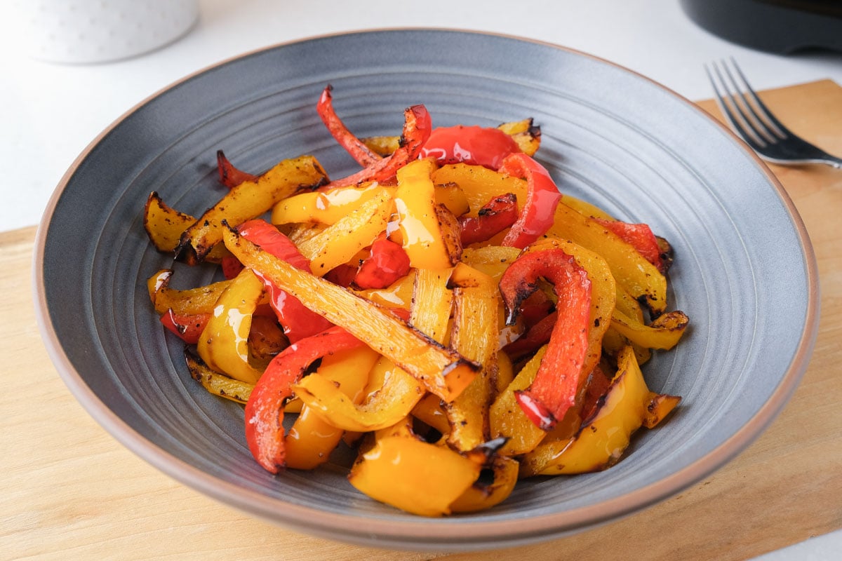 cooked strips of yellow and red peppers in blue bowl on wooden board in kitchen.