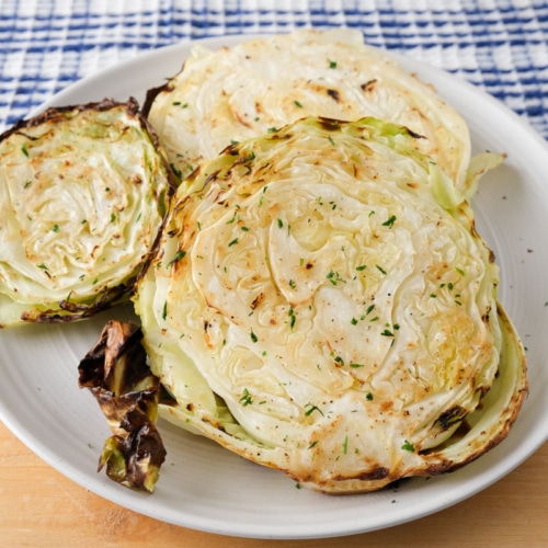 cooked cabbage steaks on white plate sitting on wooden board.