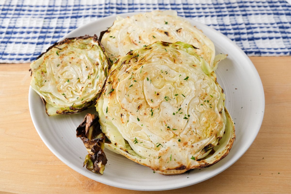 cooked cabbage steaks on white plate sitting on wooden board.