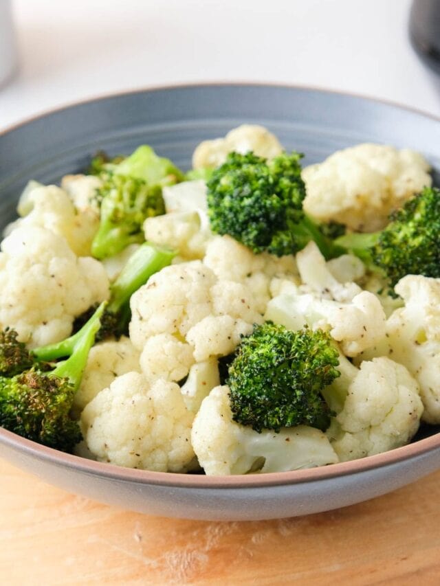 cooked broccoli and cauliflower florets in blue bowl on wooden board on counter.