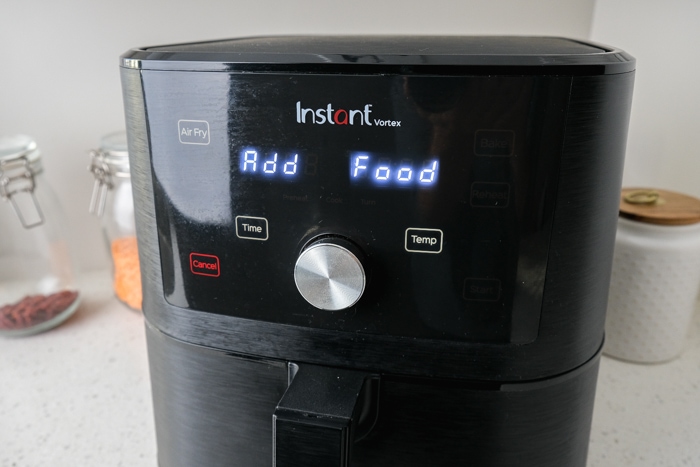 black air fryer on kitchen counter with "add food" on the display.