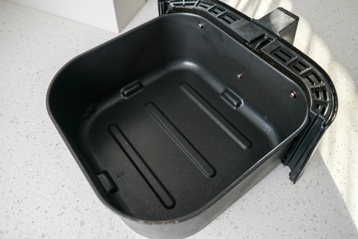black metal air fryer basket without tray on white counter top.