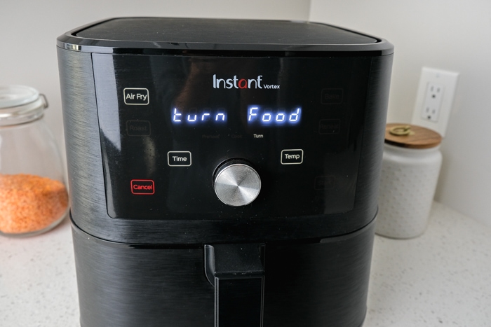 black air fryer on kitchen counter displaying "turn food" on screen.