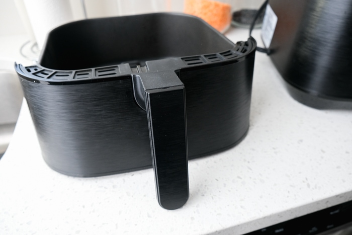 black air fryer basket with plastic handle on counter beside air fryer.