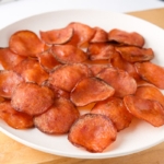 white plate full of crispy pepperoni sitting on wooden serving board.