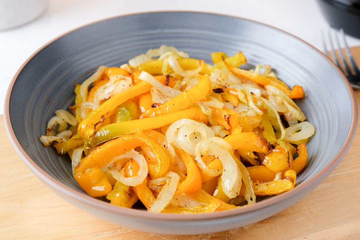 air fried onions and yellow peppers in blue bowl on wooden board.