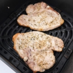 two cooked pork chops in black air fryer basket on white countertop.