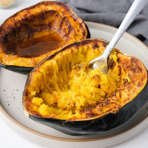 two halves of acorn squash with silver fork sticking out on beige plate on counter.