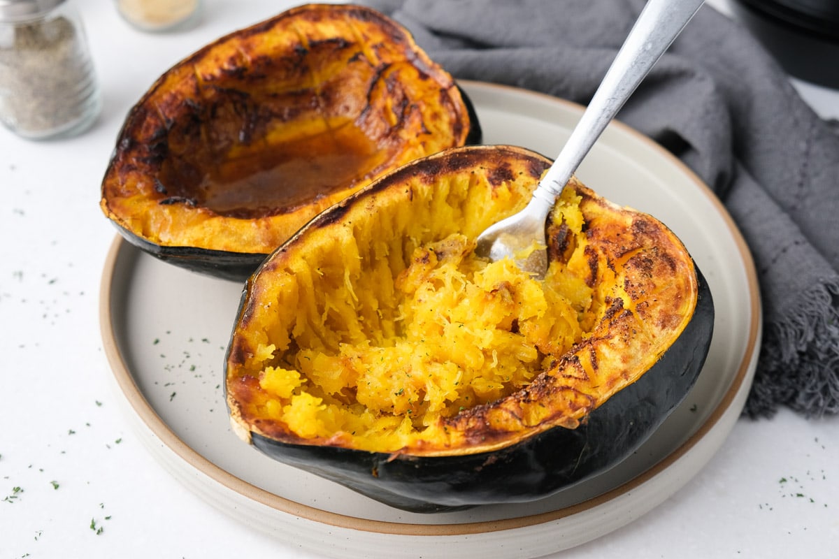 two halves of acorn squash with silver fork sticking out on beige plate on counter.