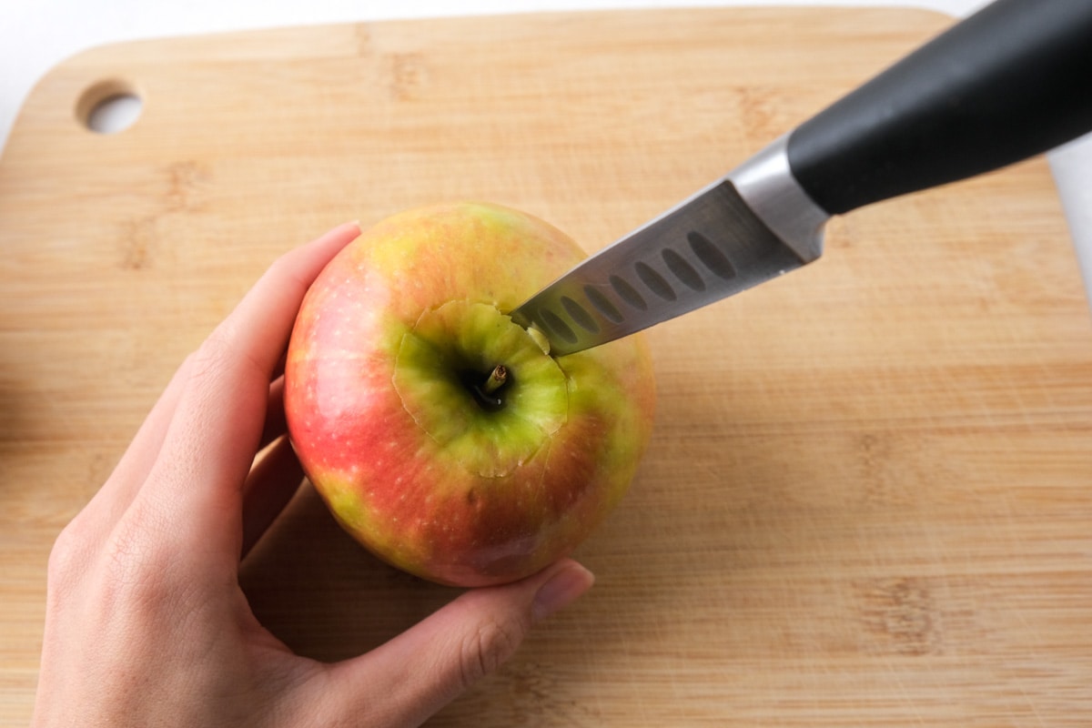 knife sticking out of red apple held in hand over wooden board.