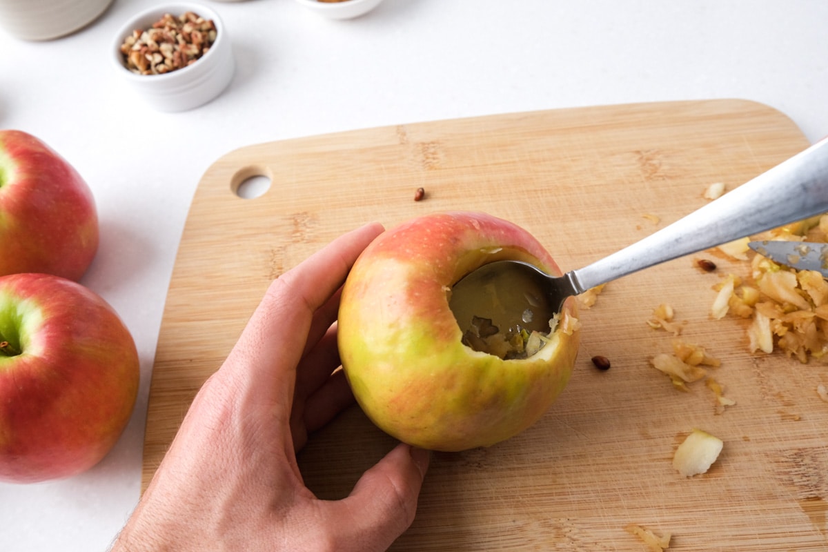 spoon taking core out of apple on top of wooden cutting board.