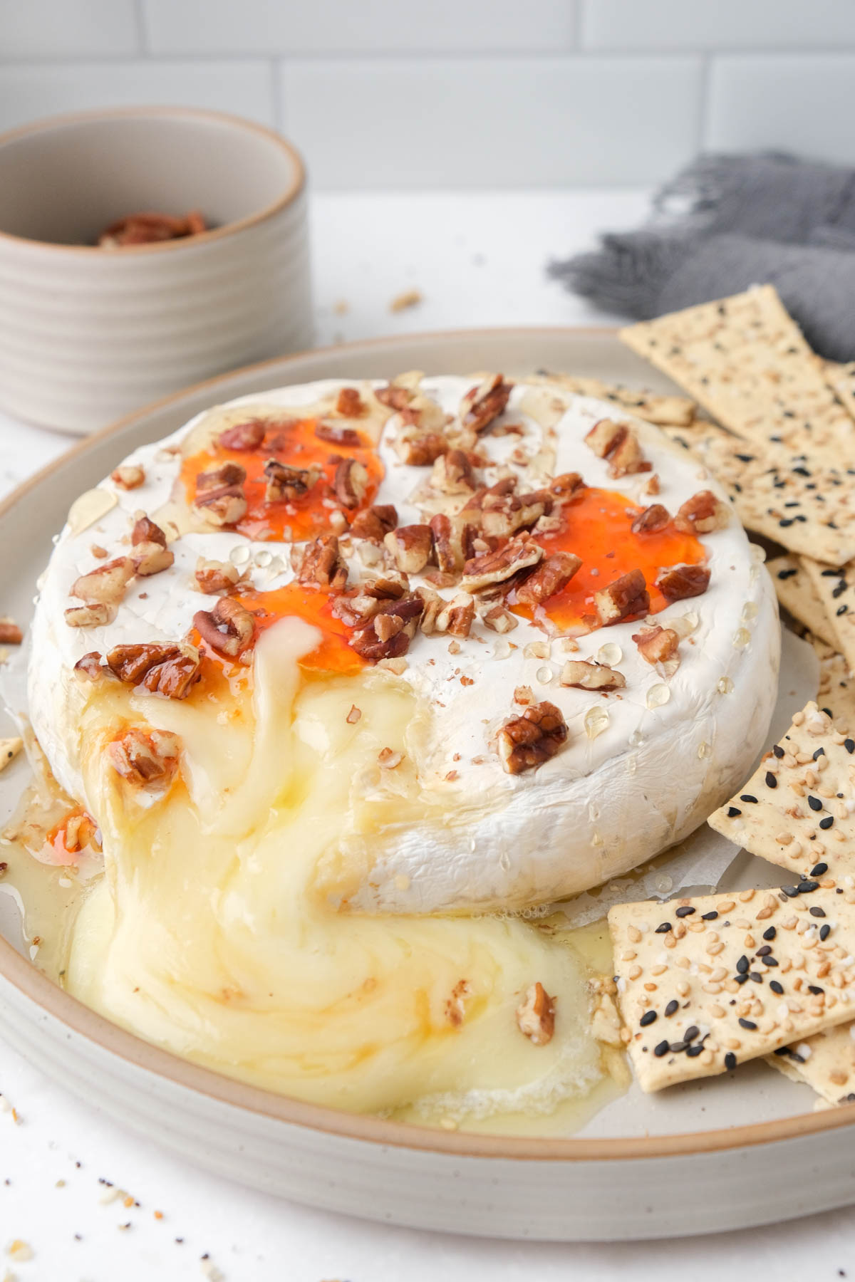 baked brie covered in toppings with cheese flowing out onto plate.