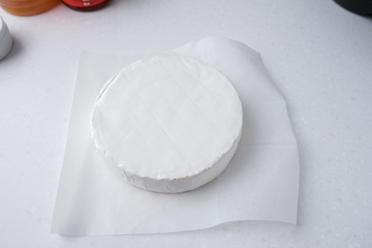 round white brie cheese on parchment paper on white counter top.