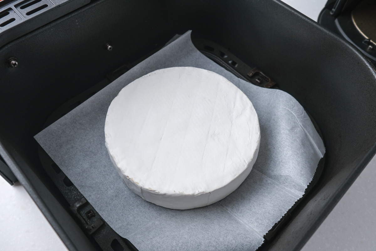 round brie cheese on parchment paper in black air fryer basket.