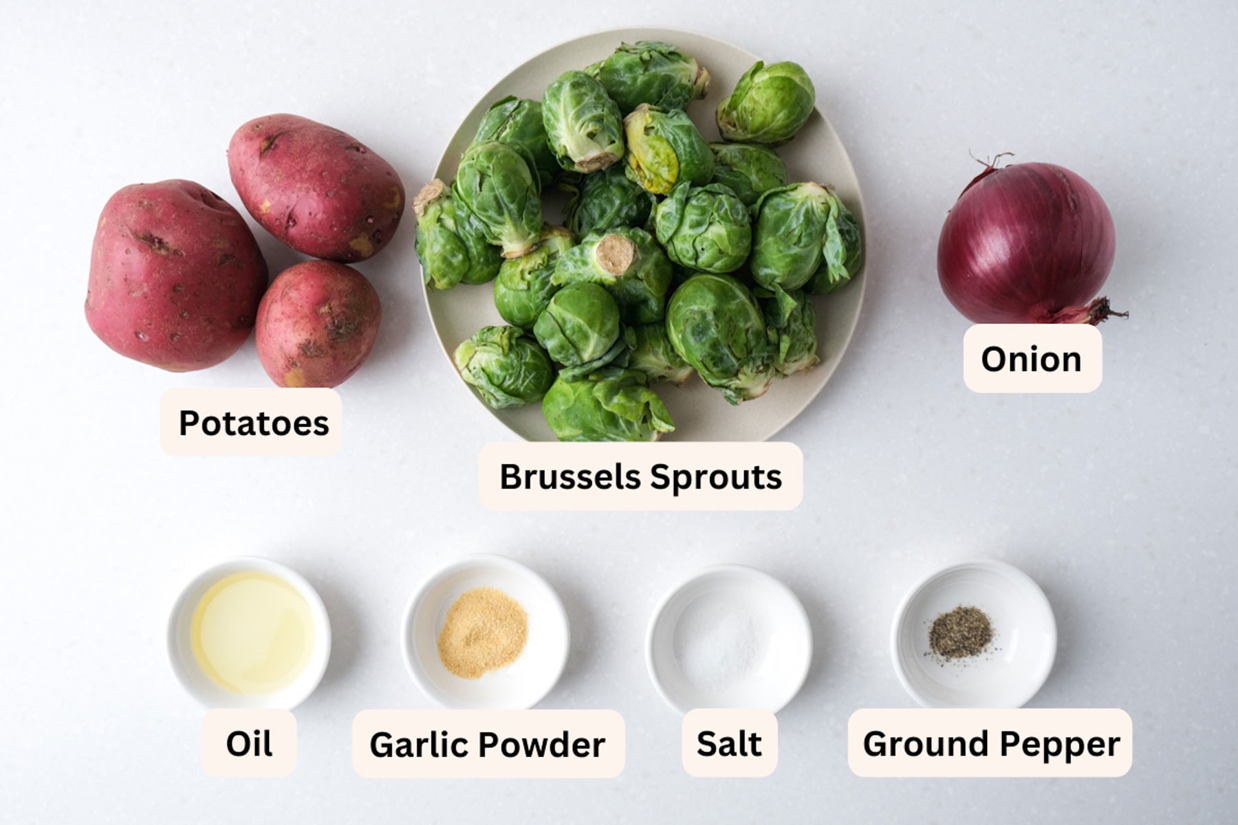 ingredients for brussels sprouts and potatoes in white dishes on counter top with labels.