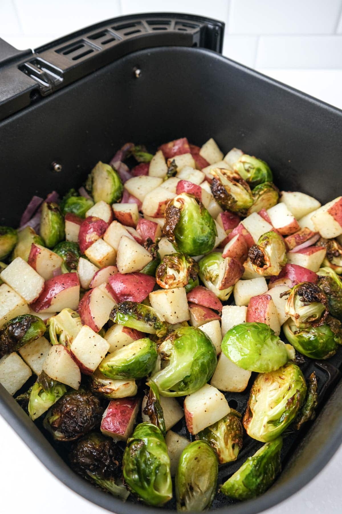 air roasted brussels sprouts and potatoes in black air fryer tray on counter top.