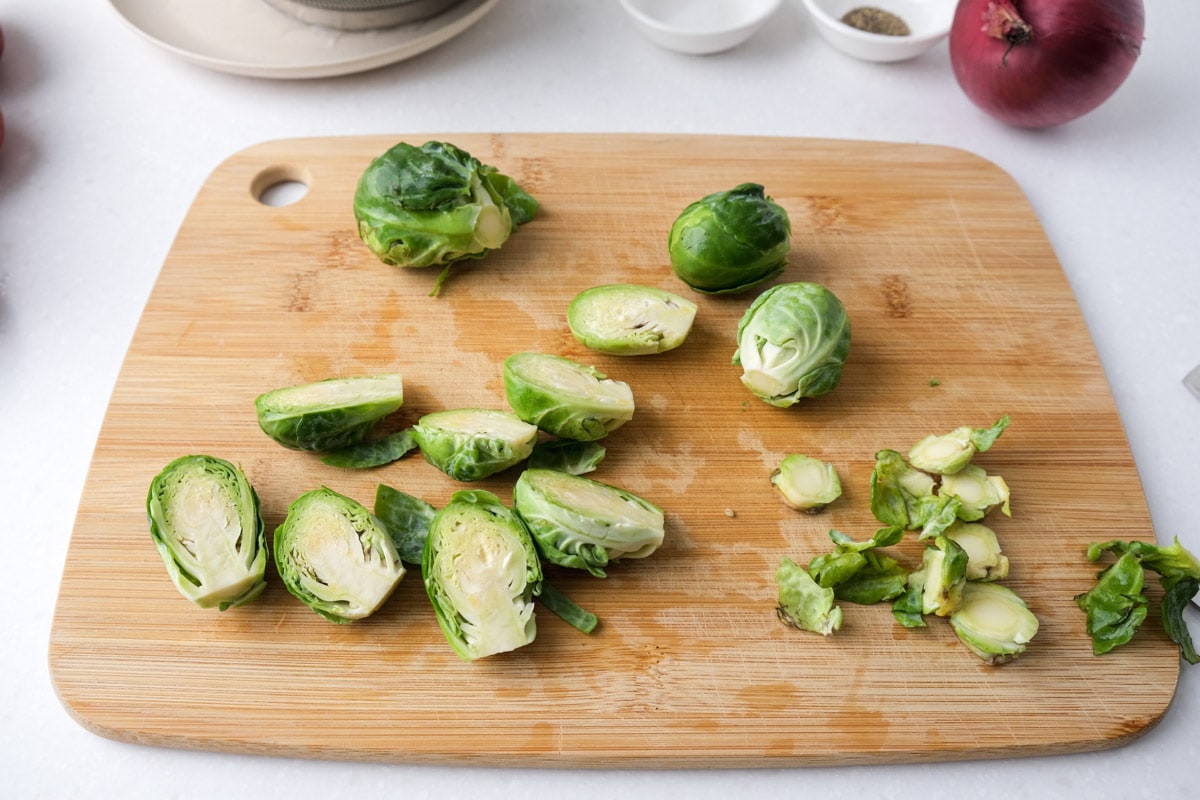 brussels sprouts cut up on wooden cutting board with things around on the kitchen counter.