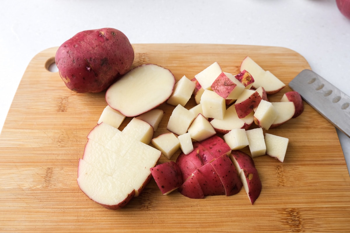 red potatoes cut into chunks on wooden cutting board on white counter.