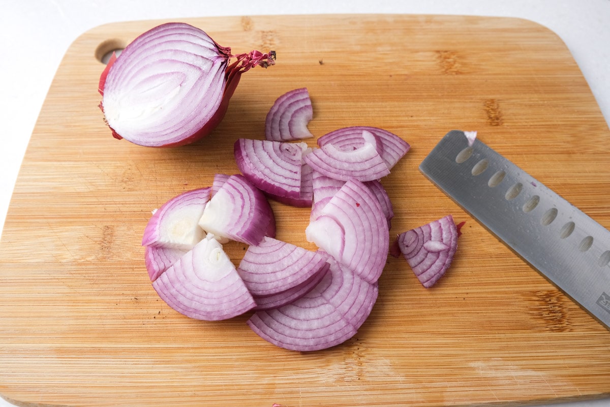 red onion cut into slices with knife beside on wooden cutting board.