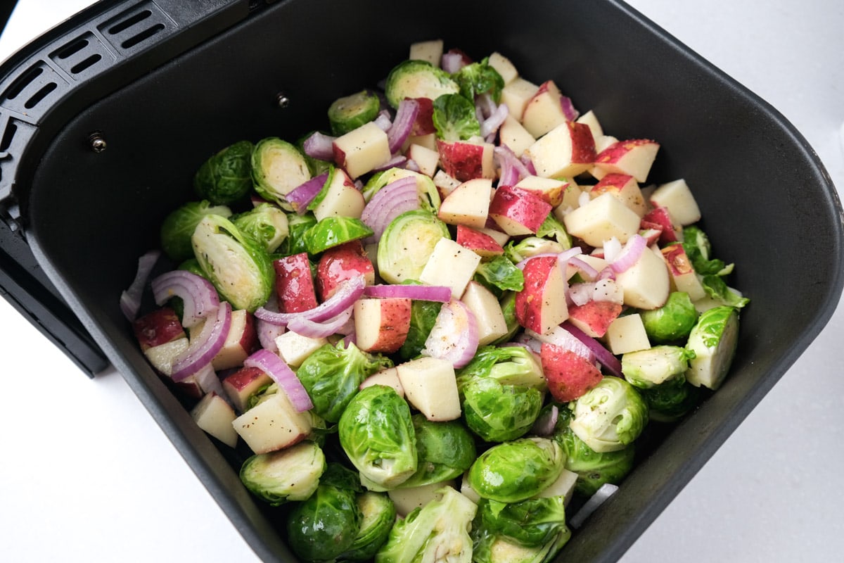 brussels sprouts and red potatoes in black air fryer tray sitting in white counter.