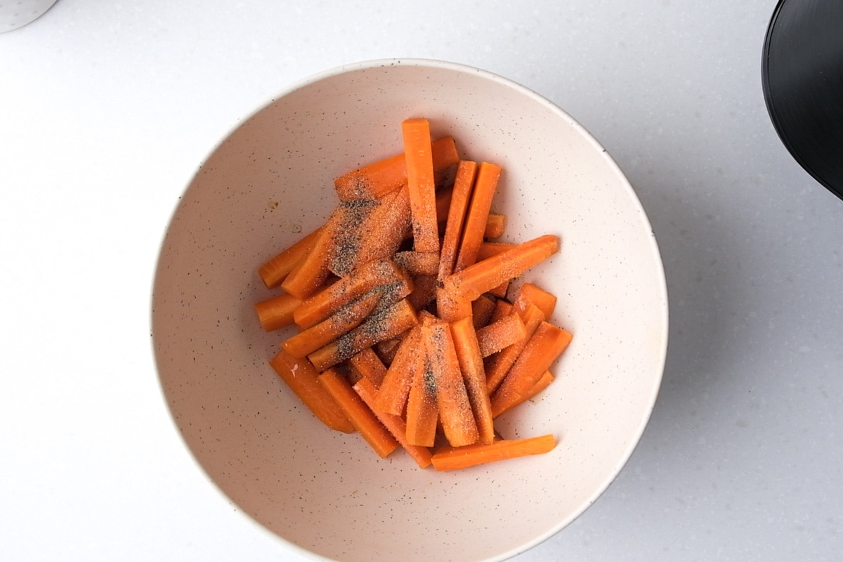 cut carrots covered in spices in white mixing bowl on counter top.