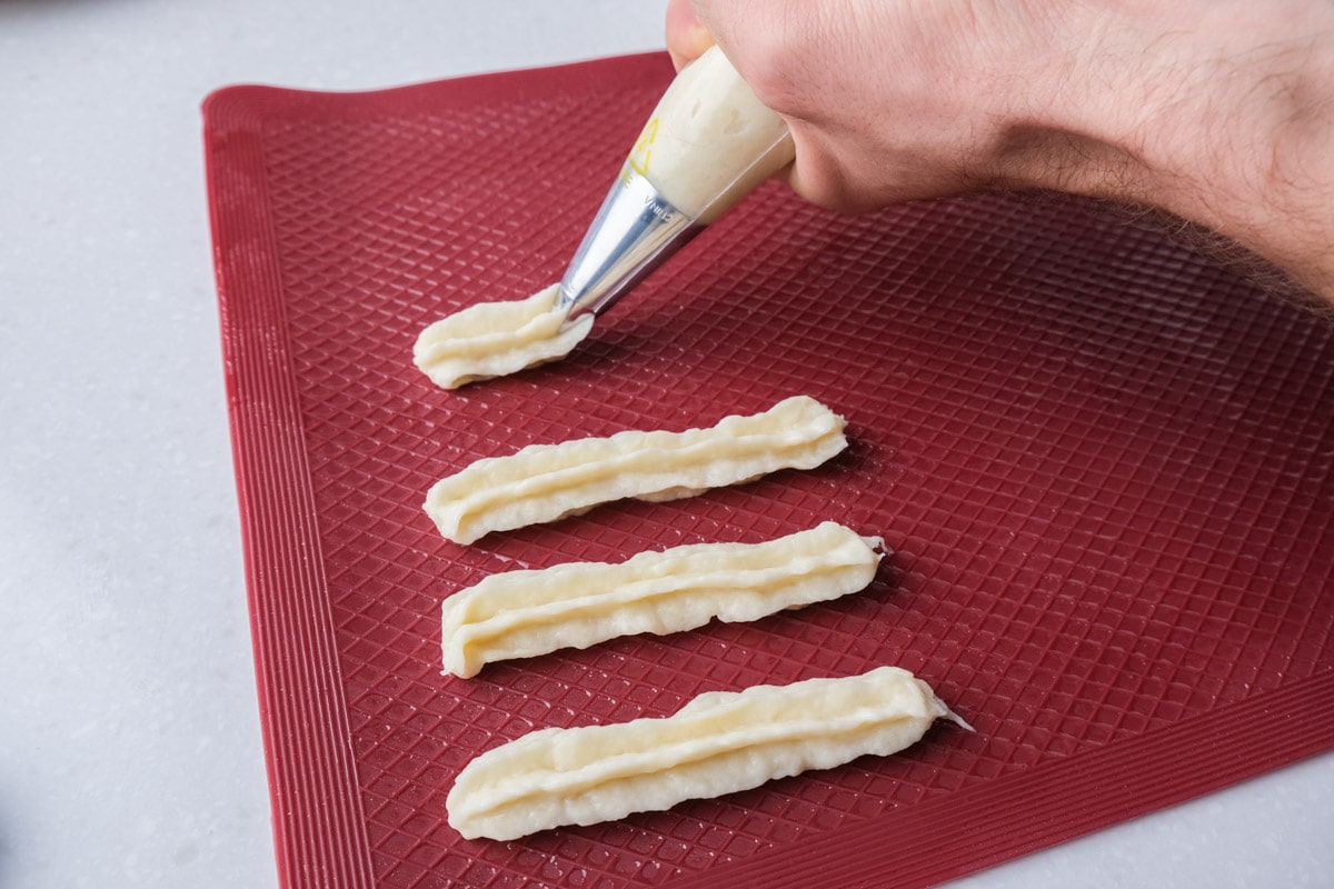 piping raw churros onto red silicone mat.