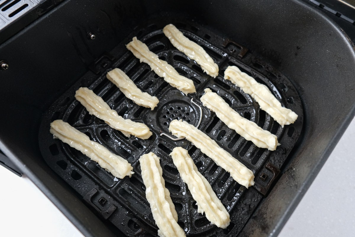 two rows of raw churros in black air fryer tray on white counter.