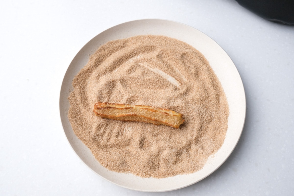 cooked churros on plate covered in cinnamon and sugar mix.