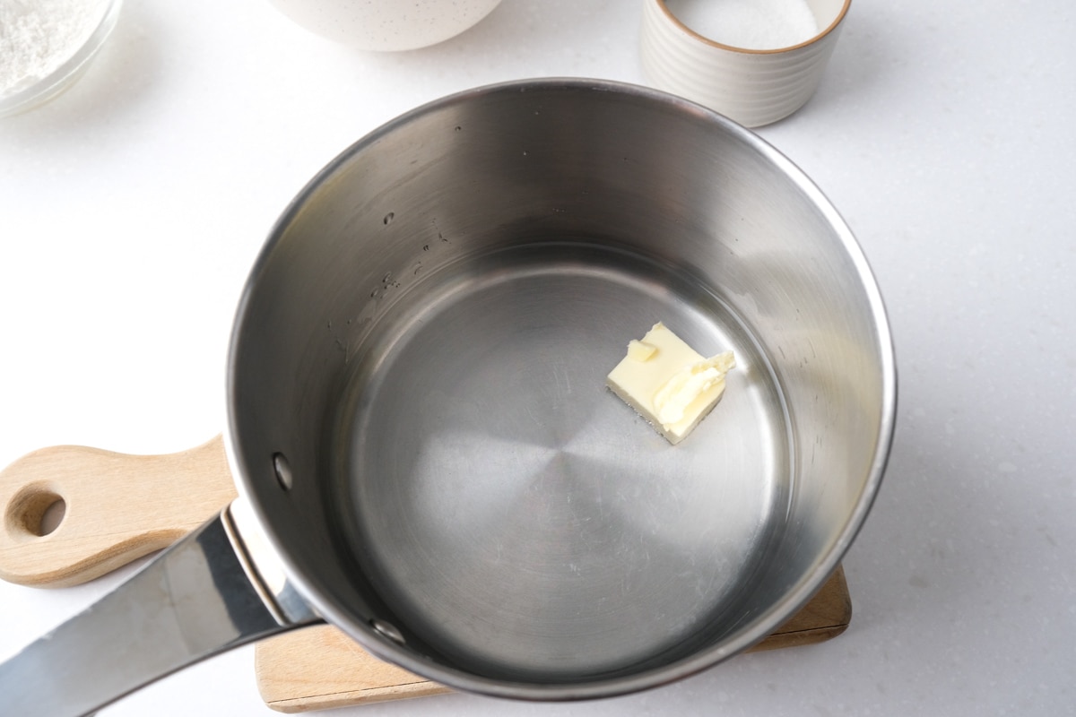 butter and water in metal sauce pan sitting on wooden board on counter top.