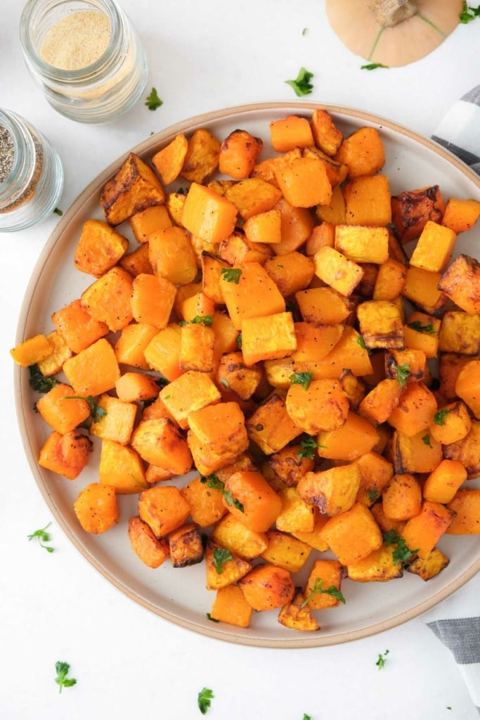 orange cubes of butternut squash on circle plate with chopped parsley around on counter.