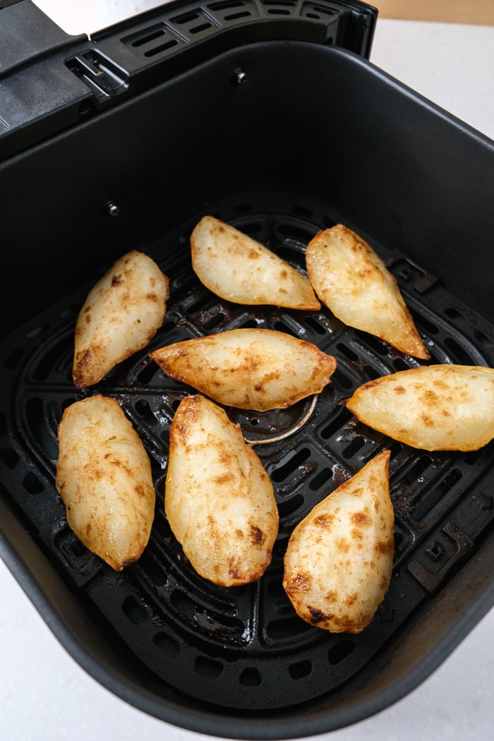 black air fryer basket filled with golden brown baked pears.