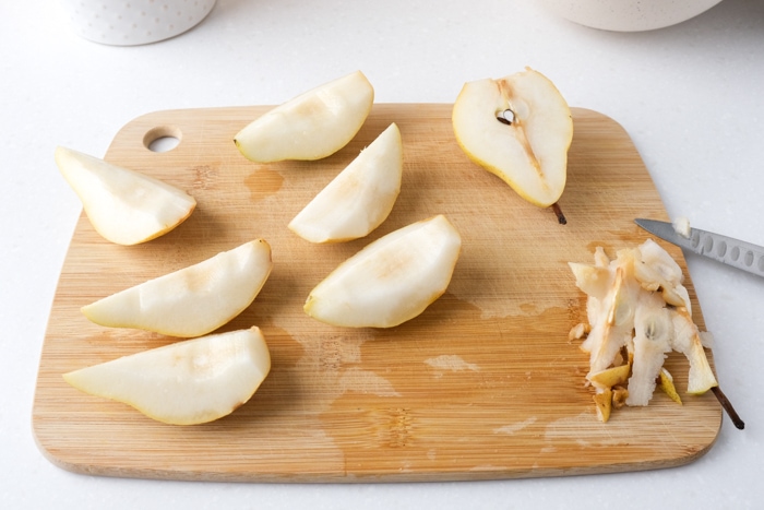 pears cut into quarters on wooden cutting board on counter.