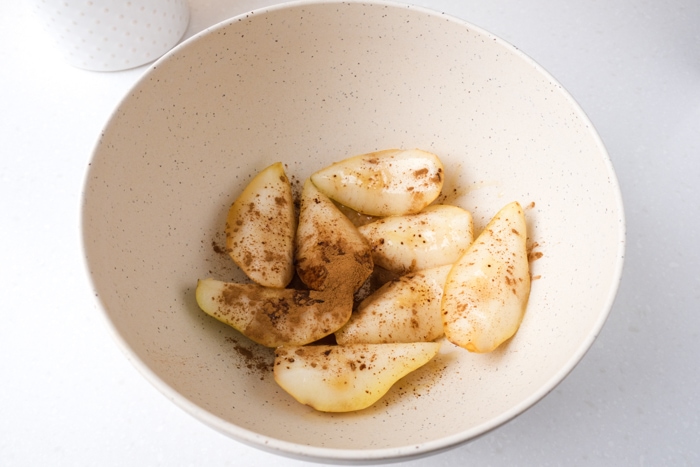 raw pears in white mixing bowl with sugar and spices covering them.