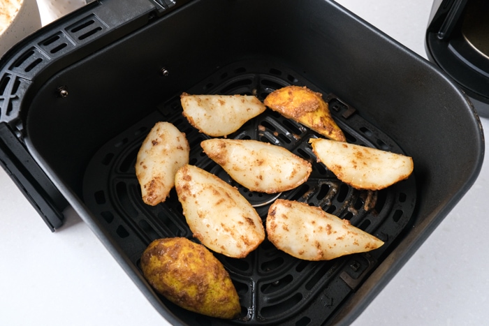 raw pieces of pear covered in sugar and spices sitting in black air fryer tray.