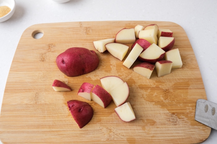 red potatoes cut into chunks on wooden cutting board with knife beside.