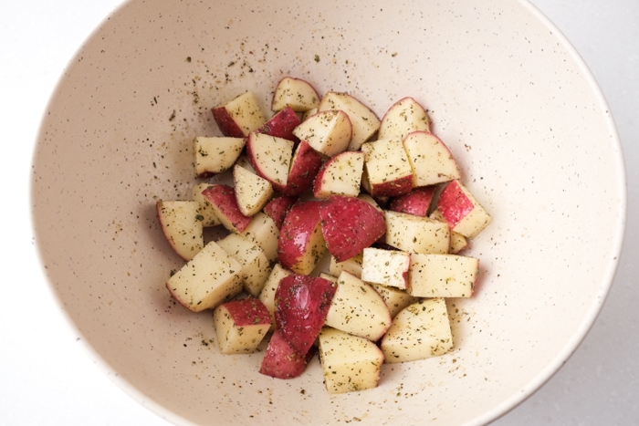 red potato cubes in white mixing bowl coated in oil and spices.