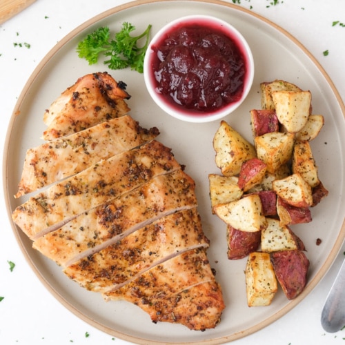 sliced cooked turkey breast on plate with potatoes and cranberries.