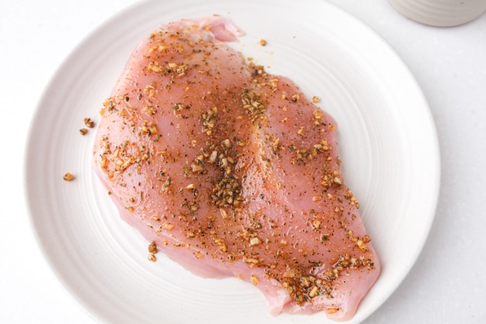 raw turkey breast on white plate covered in spices.