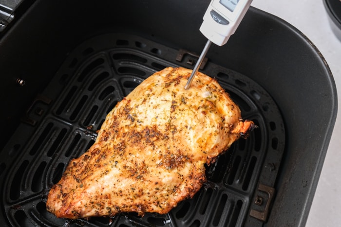 cooked turkey breast in black air fryer basket with silver thermometer sticking out.